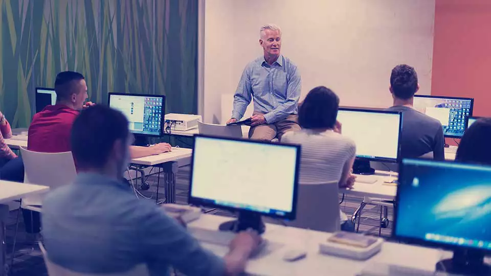 teacher sitting with students in front of computers